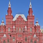 Красный фасад Исторического музея с островерхими башнями на фоне синего неба, слева башня Кремля