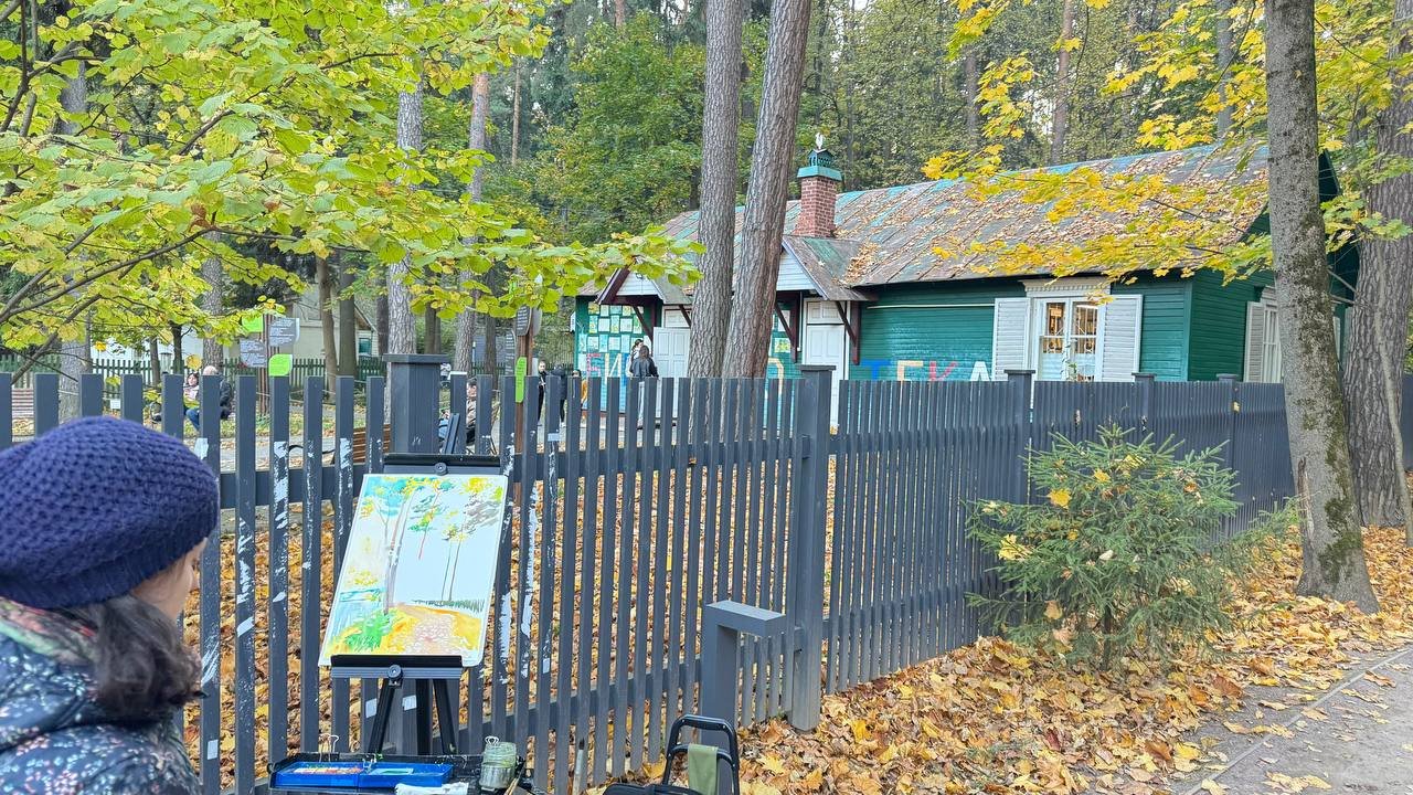 Художник у мольберта перед зелёным корпусом с надписью «Библиотека» в осеннем Переделкине