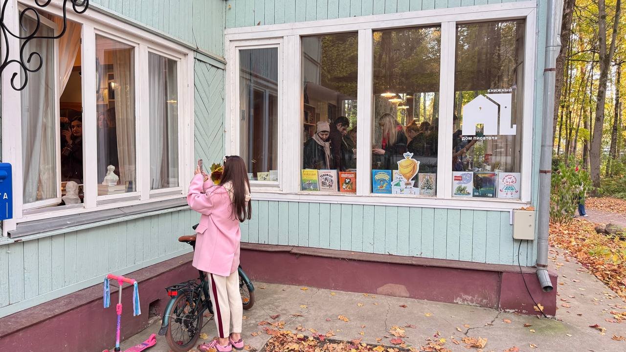 Витрина книжного «Дома писателя» с книгами в окне мятно-зелёного деревянного корпуса