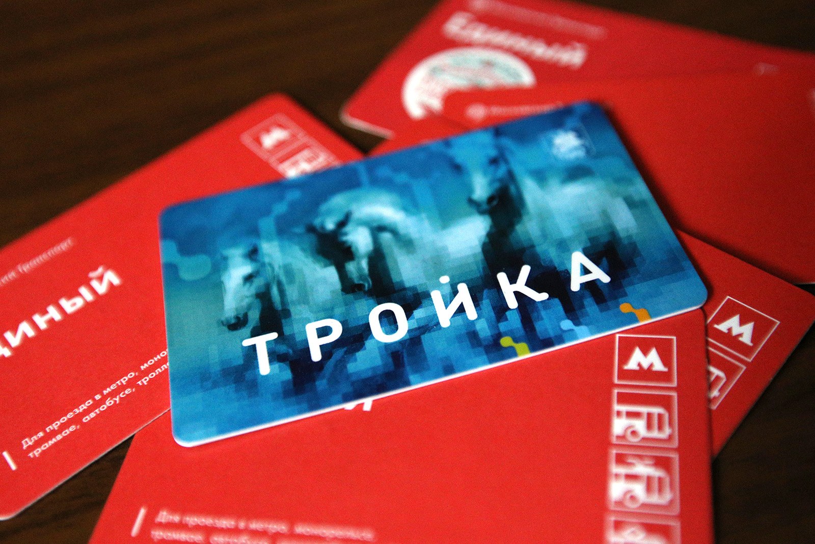 Голубая карта «Тройка» лежит на красных бумажных билетах «Единый» с логотипами метро и наземного транспорта