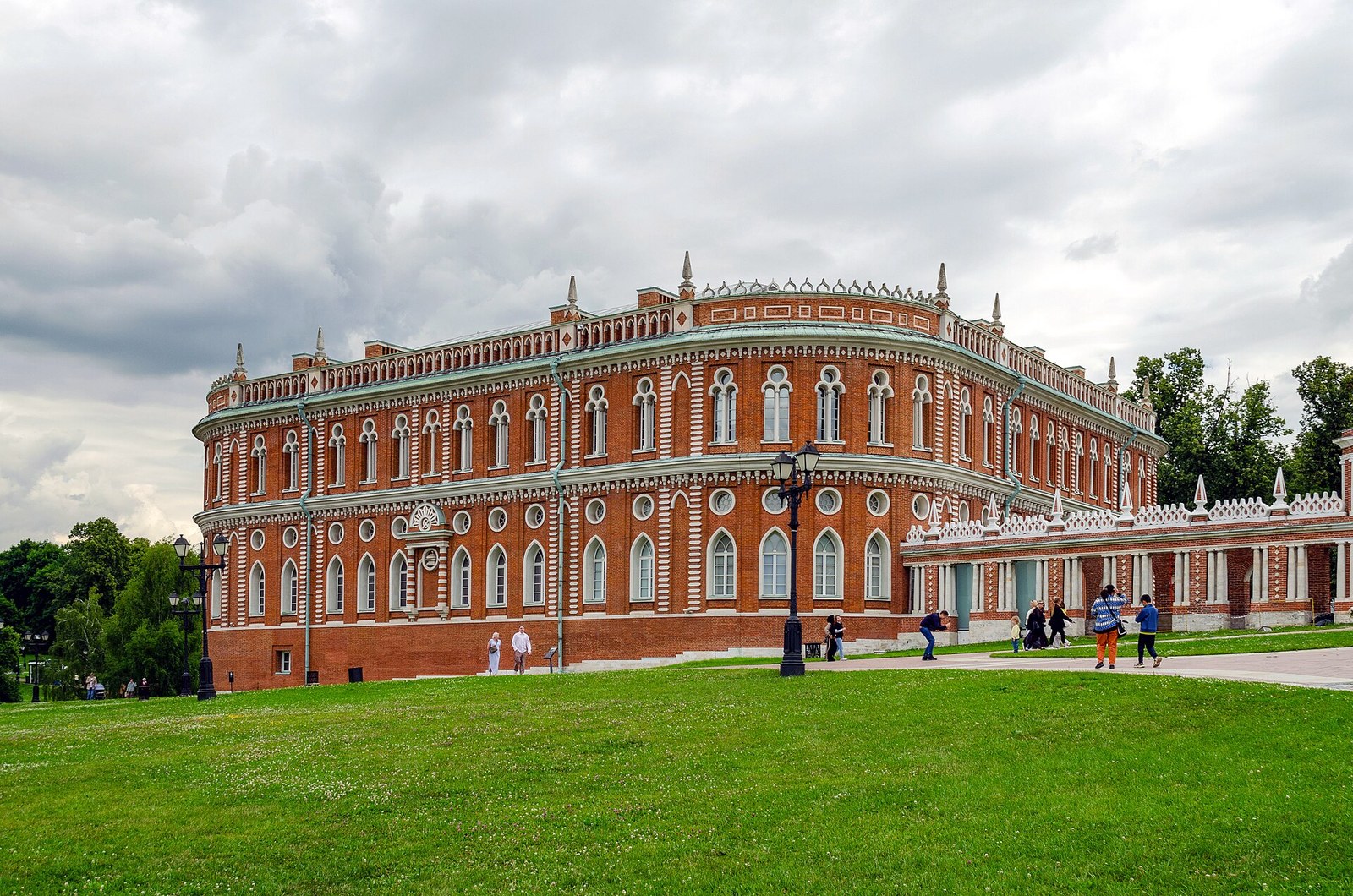 Краснокирпичное здание Хлебного дома в Царицыне с белокаменным декором и стрельчатыми окнами, перед ним зелёный газон