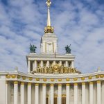 Белый Центральный павильон ВДНХ с колоннадой, золотым гербом и шпилем со звездой на фоне облачного неба